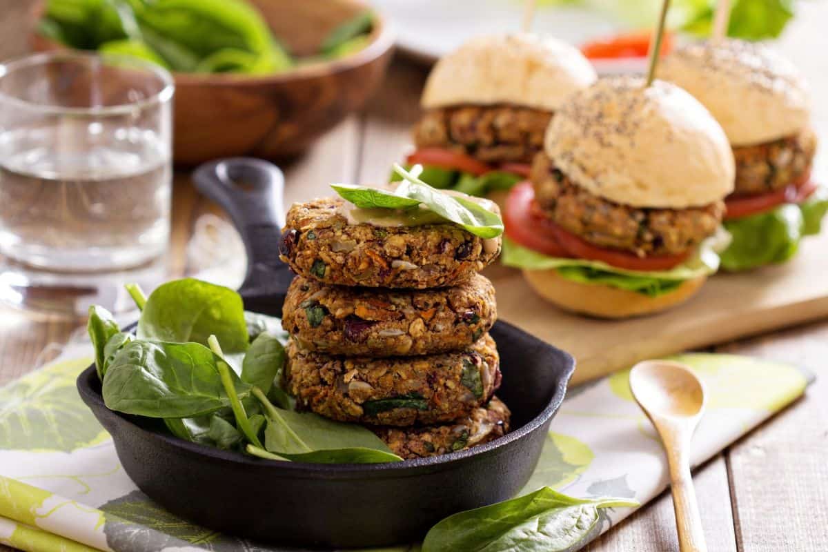 Homemade vegan patties served with spinach, with veggie burgers in the background.