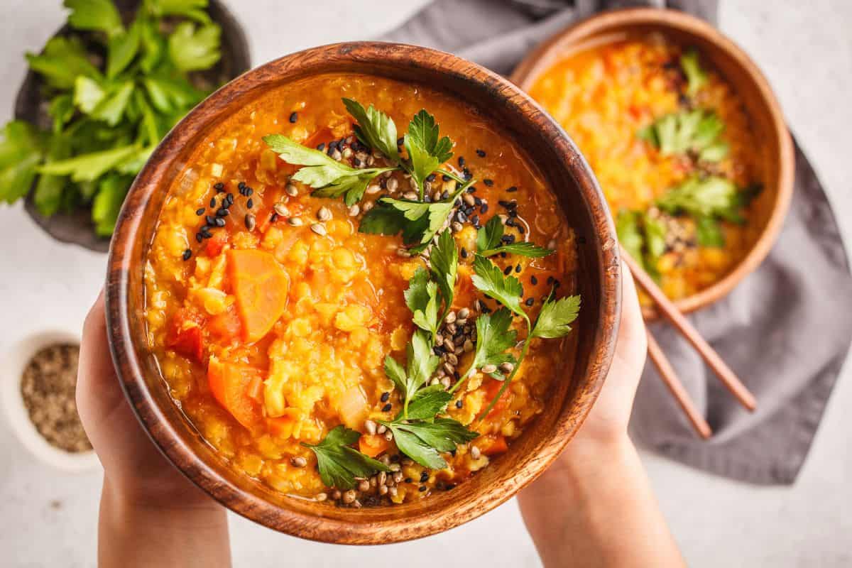 Bowls of hearty red lentil curry topped with fresh herbs and seeds.