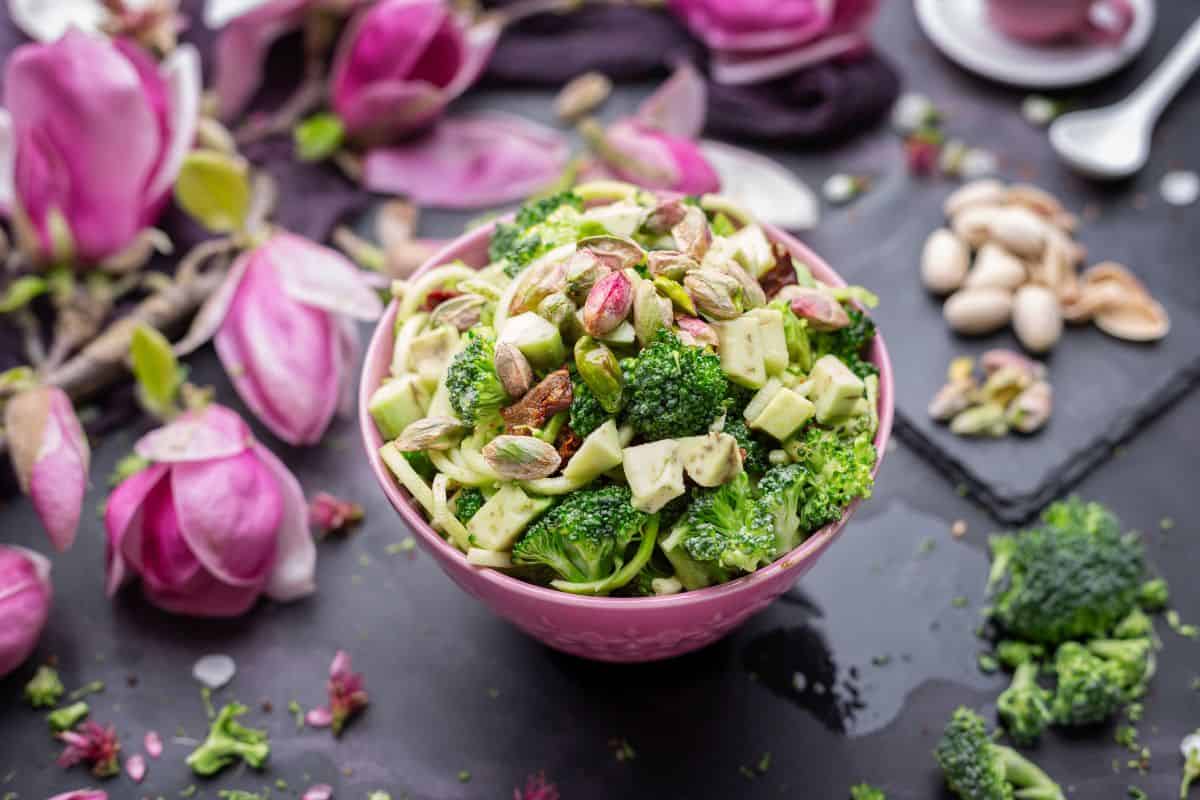 Fresh broccoli salad with avocado, nuts, and seeds served in a pink bowl.