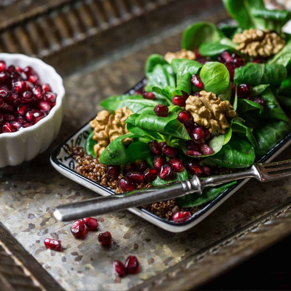 Spinach salad with pomegranate seeds, walnuts, and quinoa served on a dark plate.