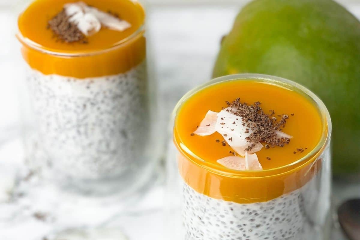 Mango chia pudding in glass cups topped with mango puree and coconut flakes.