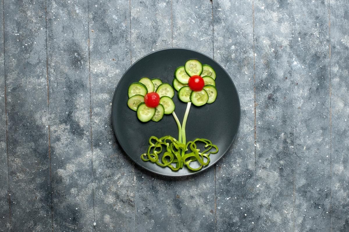 A black plate with cucumber slices, cherry tomatoes, and green peppers arranged into decorative flowers.