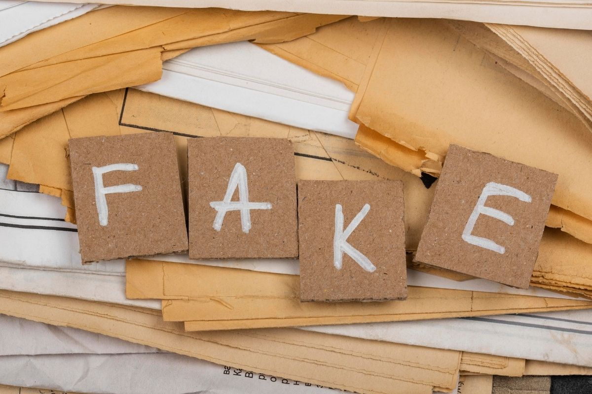 Cardboard squares spelling the word “FAKE” placed on a pile of old paper documents.