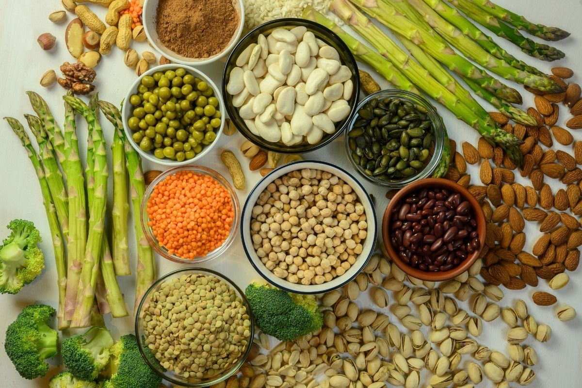 An overhead view of plant-based protein sources, including beans, lentils, chickpeas, nuts, seeds, asparagus, and broccoli.