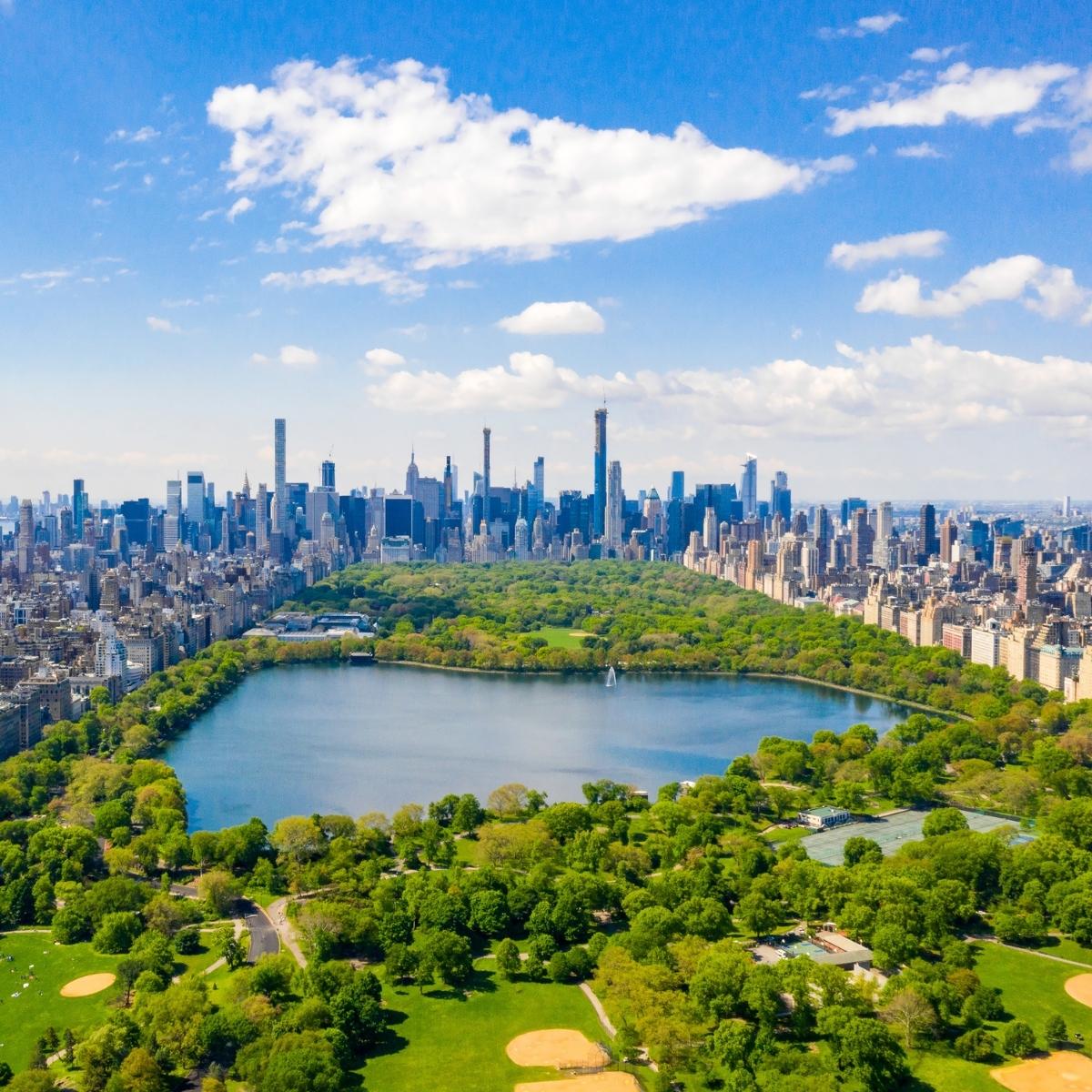 Aerial view of Central Park in New York City, featuring a large lake, lush green trees, and the Manhattan skyline.