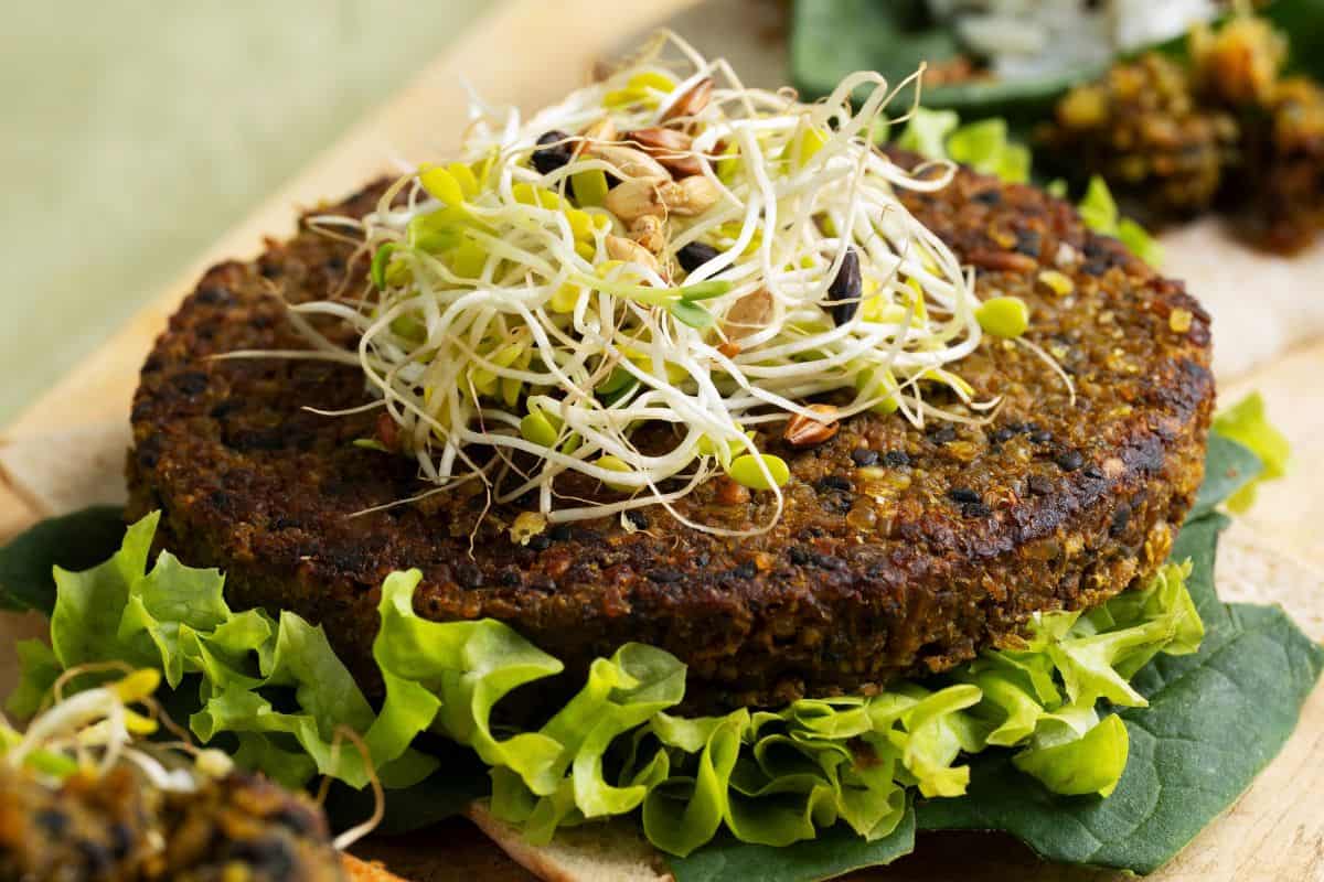 Cooked plant-based burger patty topped with fresh sprouts and served on leafy greens.