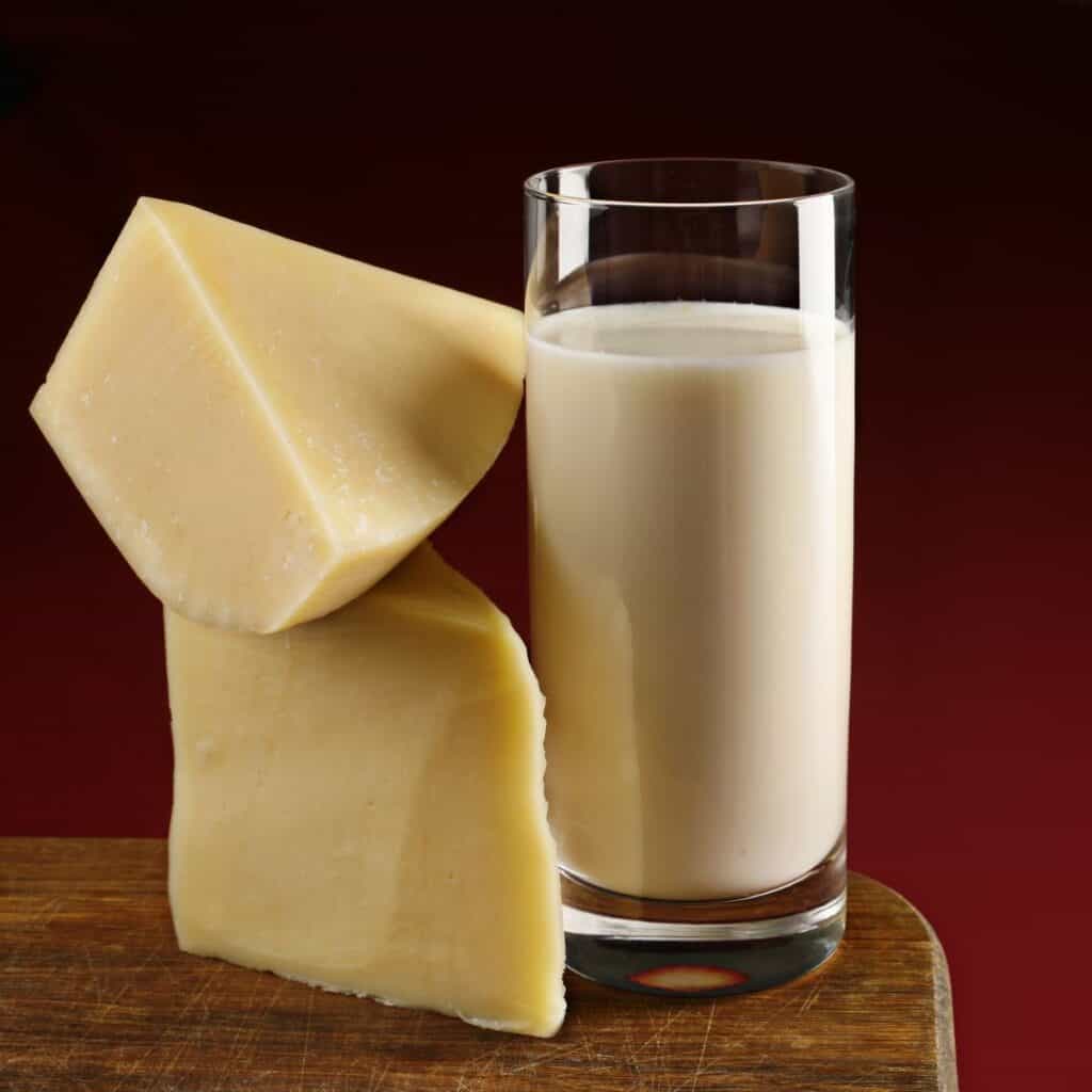 A glass of milk is placed on a wooden board next to two stacked wedges of cheese.