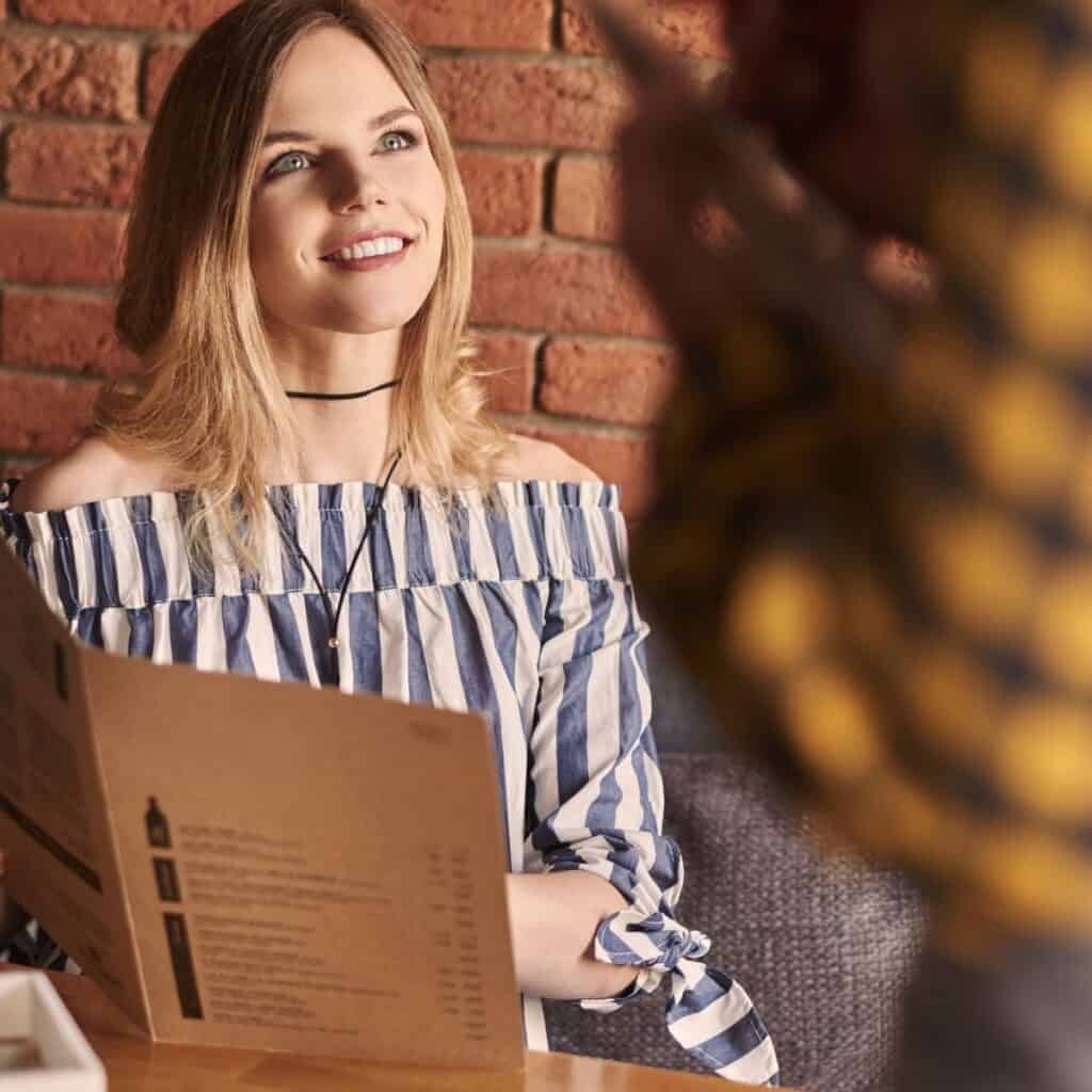 Woman sitting at a restaurant table and looking at someone while holding a menu.