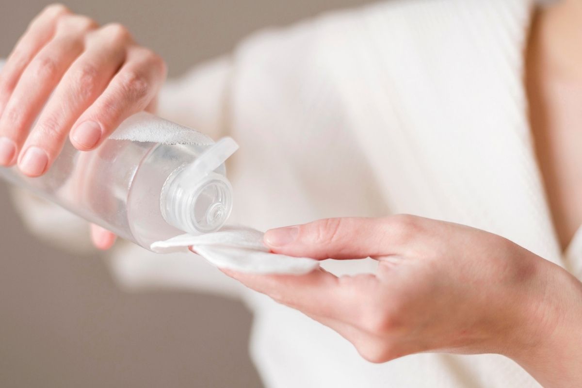 Person pouring skincare cleanser or toner onto a cotton pad.