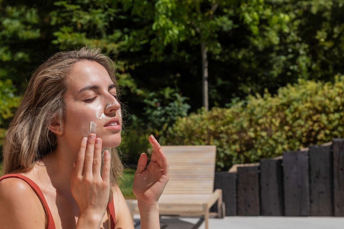 Woman applying sunscreen or face cream outdoors in the sunlight.