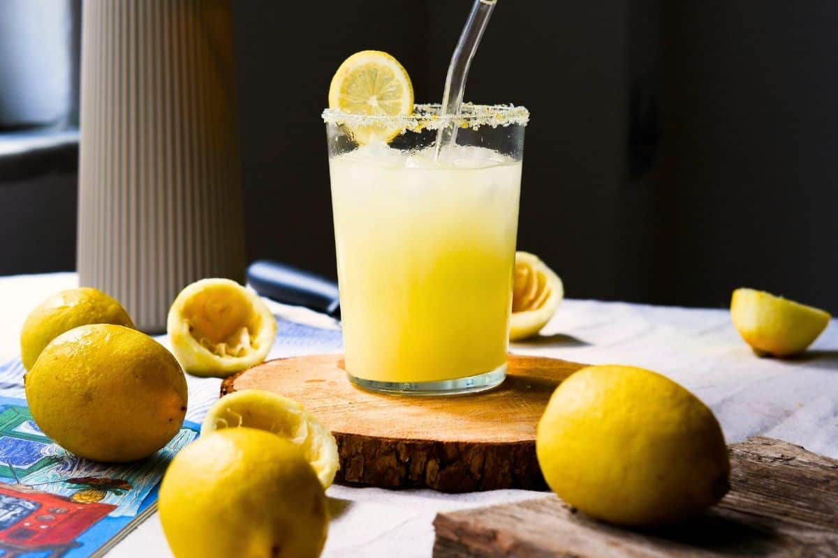 A glass of lemonade surrounded by lemons on a table