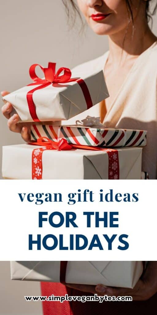 A person in a cream-colored top holding a stack of three gift-wrapped boxes with red and striped ribbons. The text overlay reads "vegan gift ideas for the holidays".