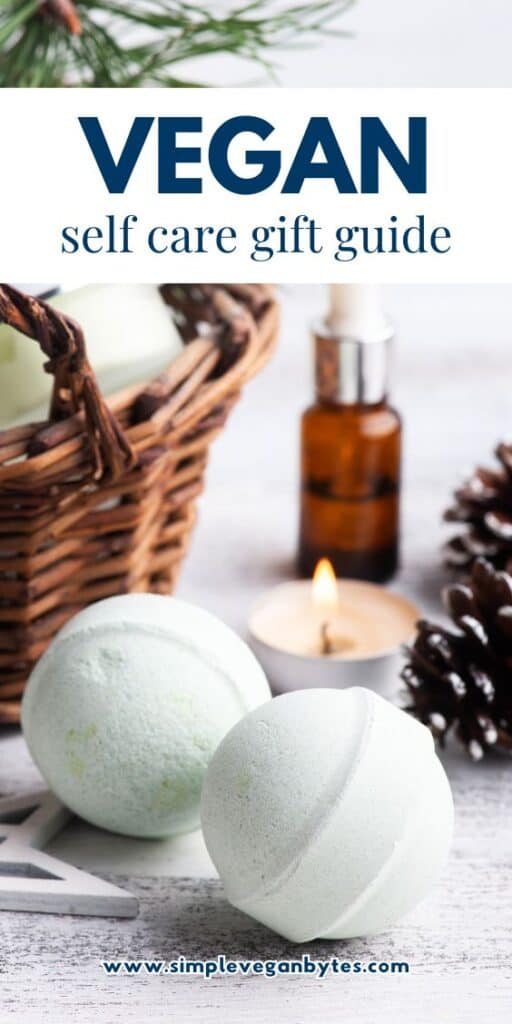 Close-up of two light green bath bombs on a wooden surface, with a wicker basket, a lit tea light candle, and pine cones in the background. The text overlay reads "Vegan self care gift guide."