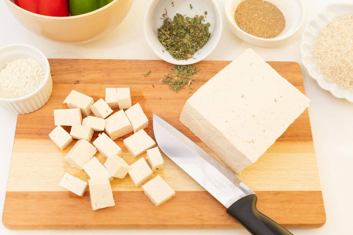 Cubed tofu on a cutting board with spices and a knife ready for cooking