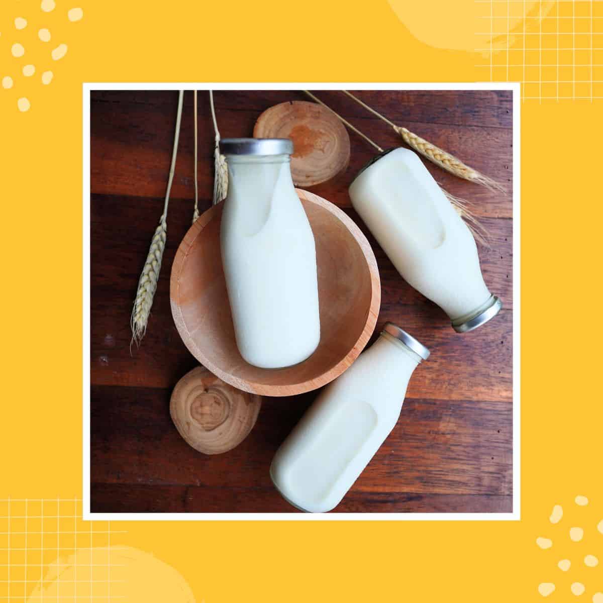 Glass bottles of milk on a wooden surface and a bowl in the background.