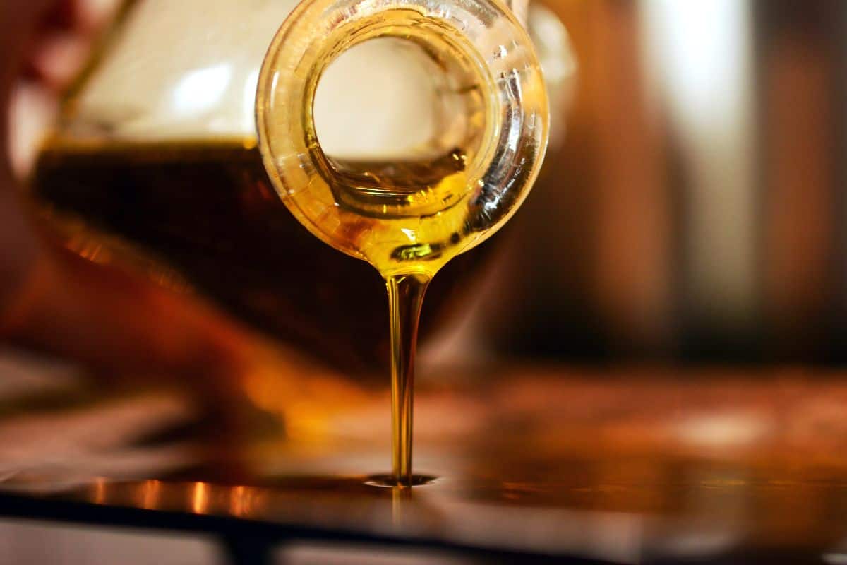 Golden oil pouring from a glass bottle onto a reflective surface.