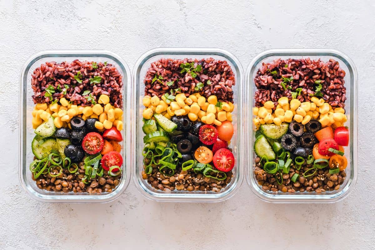 Three glass meal prep containers filled with colorful plant-based grains, vegetables, and legumes.