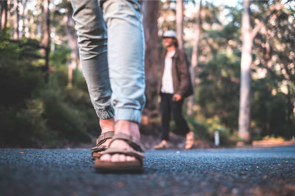 Person walking along a forest road wearing casual pants and cork sandals