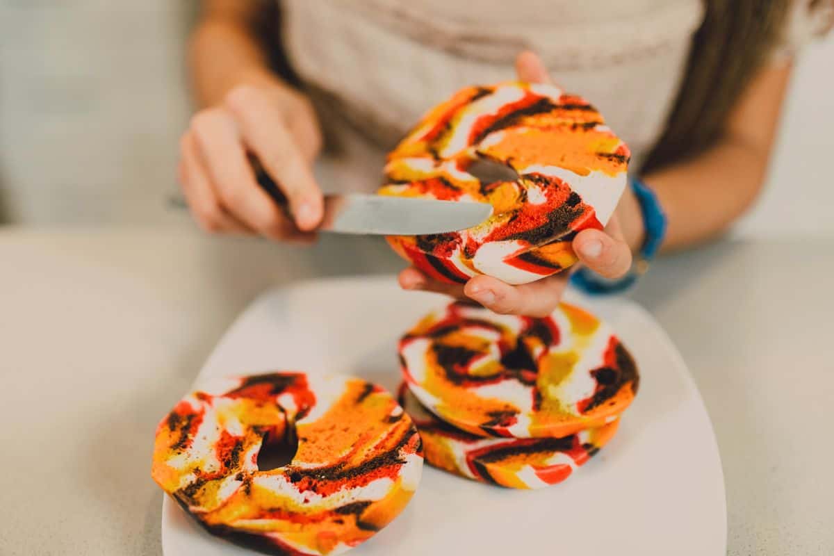 Colorful rainbow bagels being sliced for a fun vegan baking treat