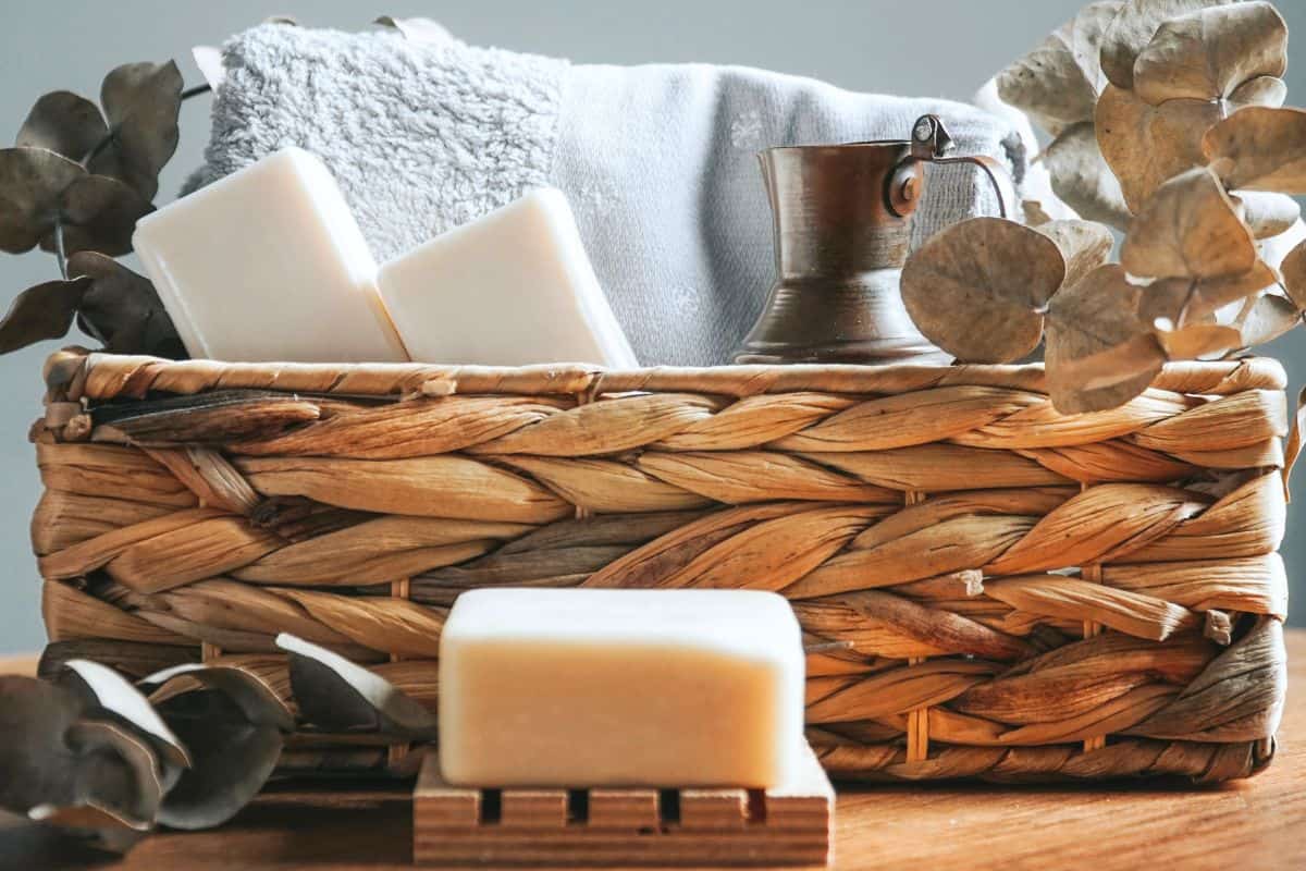 Cozy vegan holiday gift basket with candle, mug, blanket, and natural decor on a wooden table.