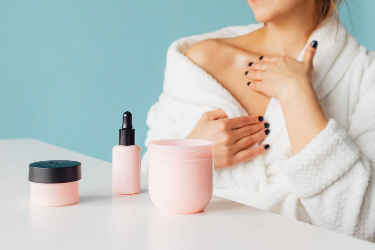 Person in robe with skincare bottles on table