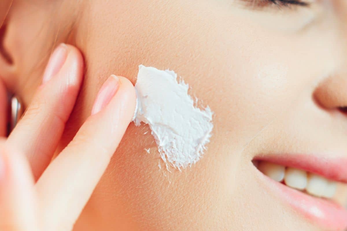 Woman applying white cream to cheek, close-up skincare routine