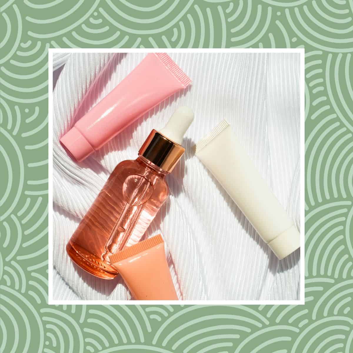 Flat lay of pink skincare dropper bottle and tubes on white fabric background