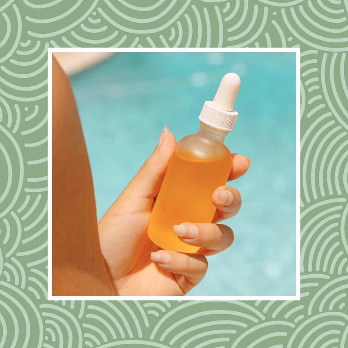Close-up of a hand holding a glass dropper bottle filled with orange serum by the pool