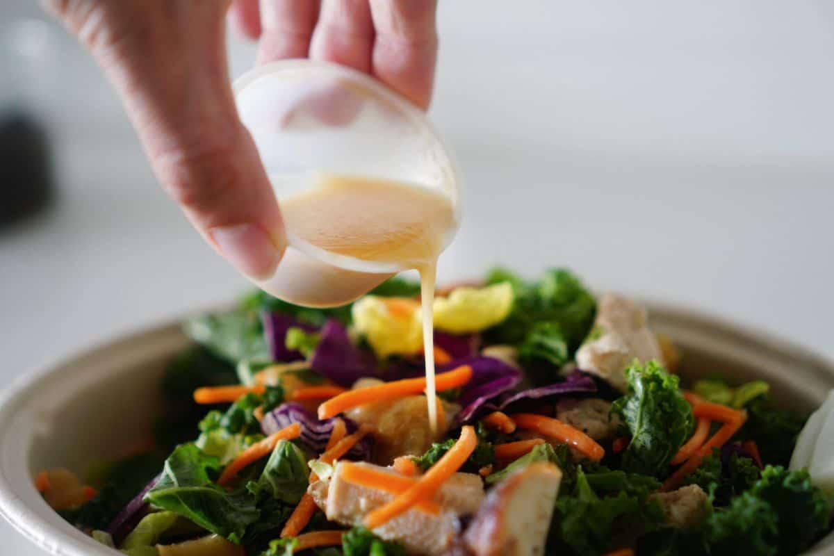 Hand pouring creamy dressing over a fresh salad bowl