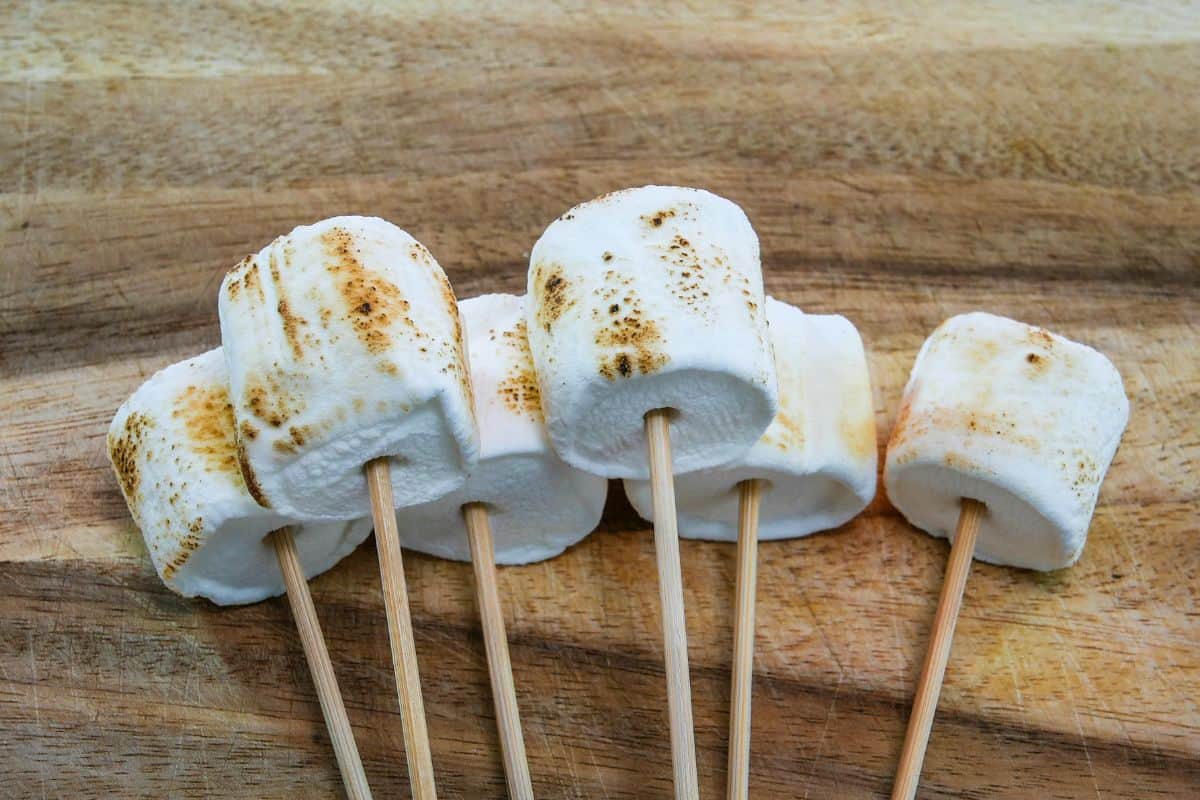 Toasted marshmallows on skewers resting on a wooden board