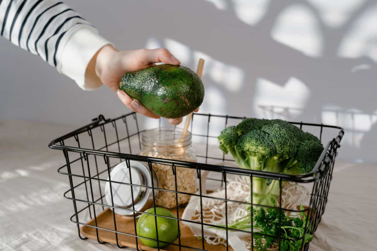 Hand placing avocado into grocery basket with vegetables