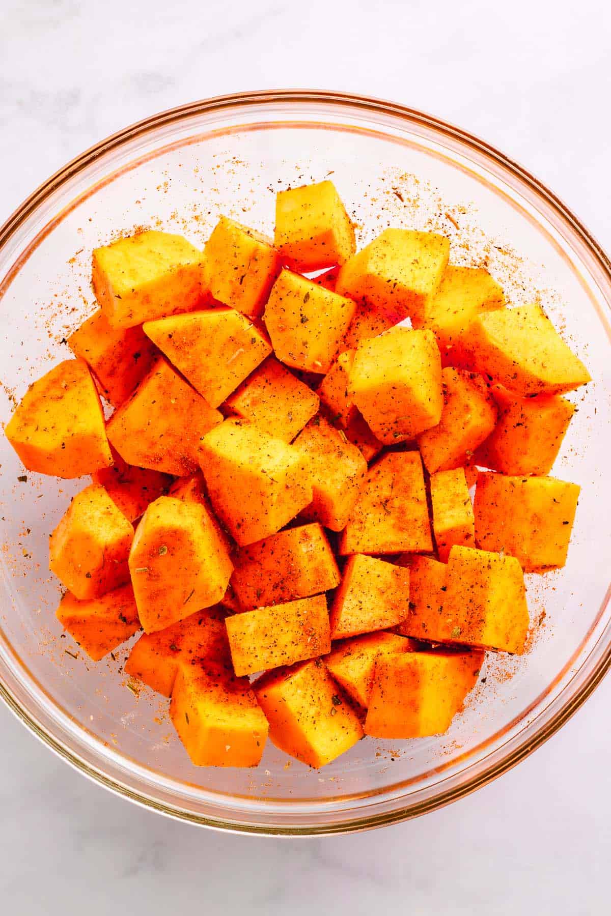 Seasoned sweet potato cubes in a glass mixing bowl