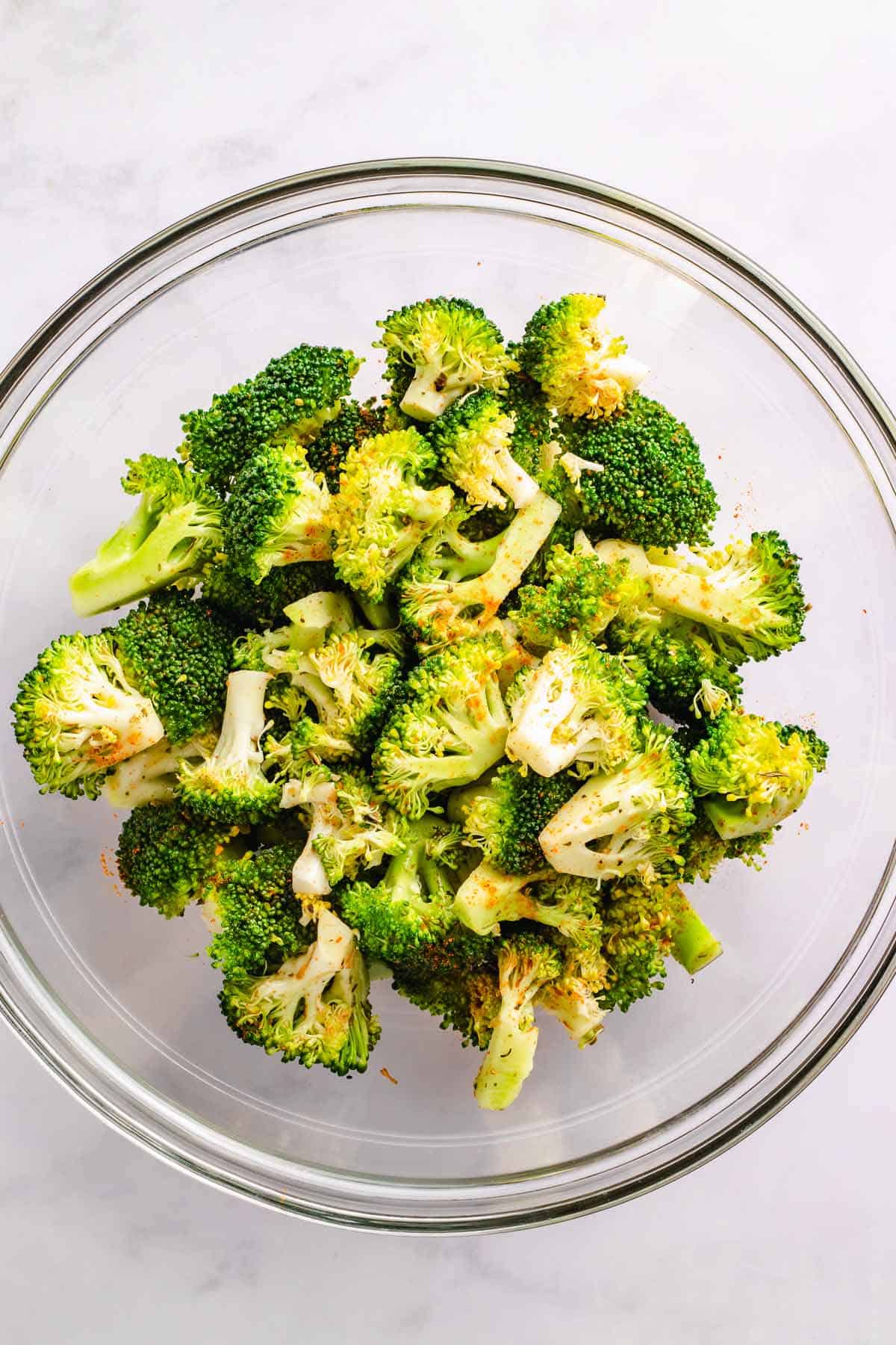 Fresh broccoli florets coated with seasoning in a glass bowl