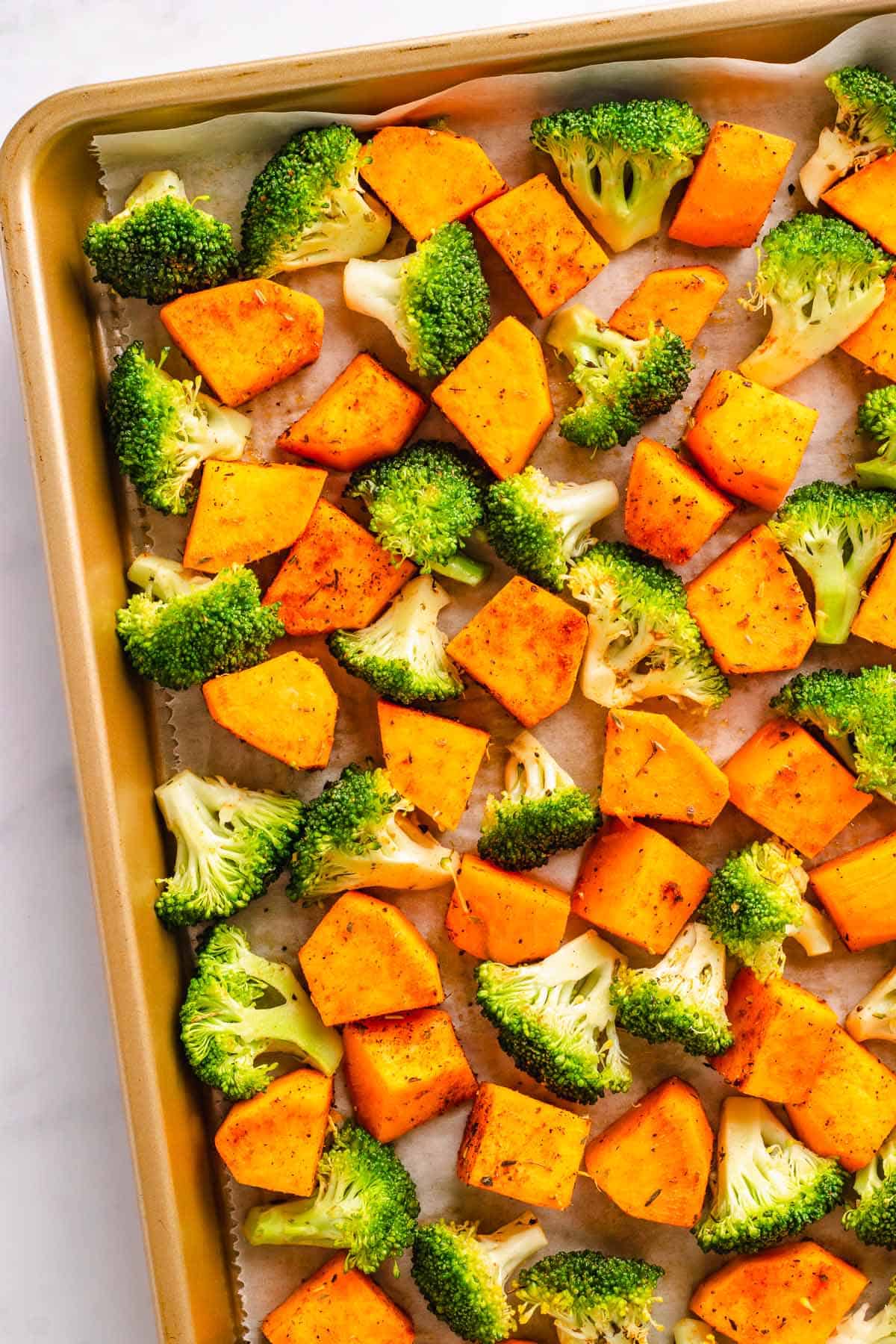 Sweet potatoes and broccoli roasting together on a sheet pan