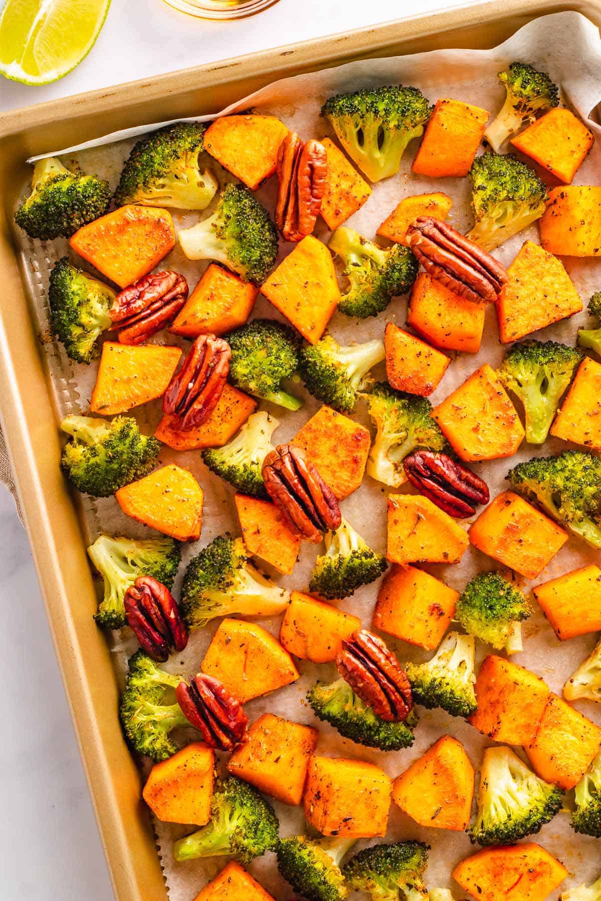 Roasted broccoli, sweet potatoes, and pecans on a baking sheet