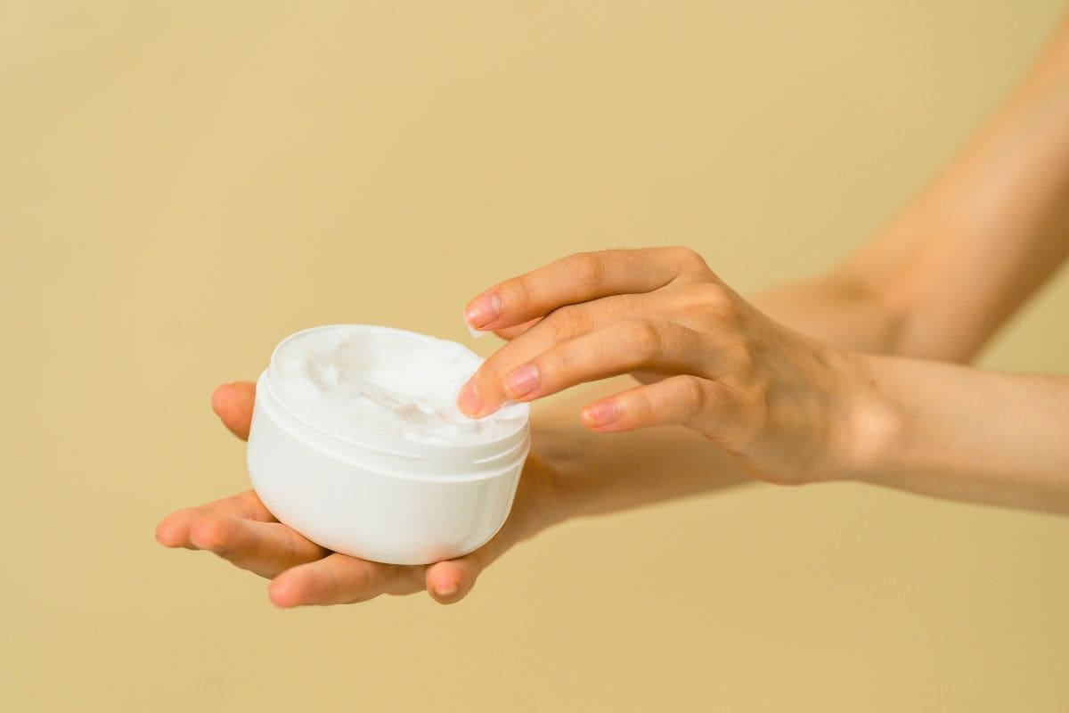 Person applying moisturizer from a white skincare jar