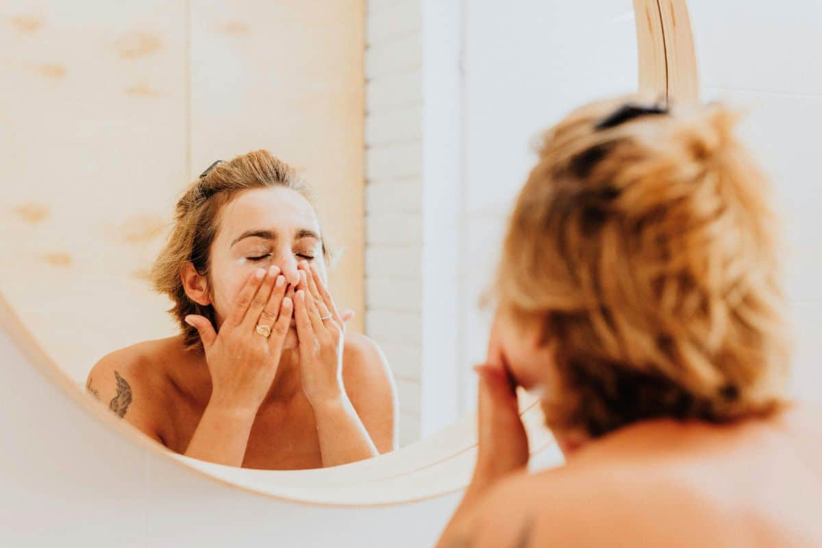 Woman washing her face in front of a bathroom mirror