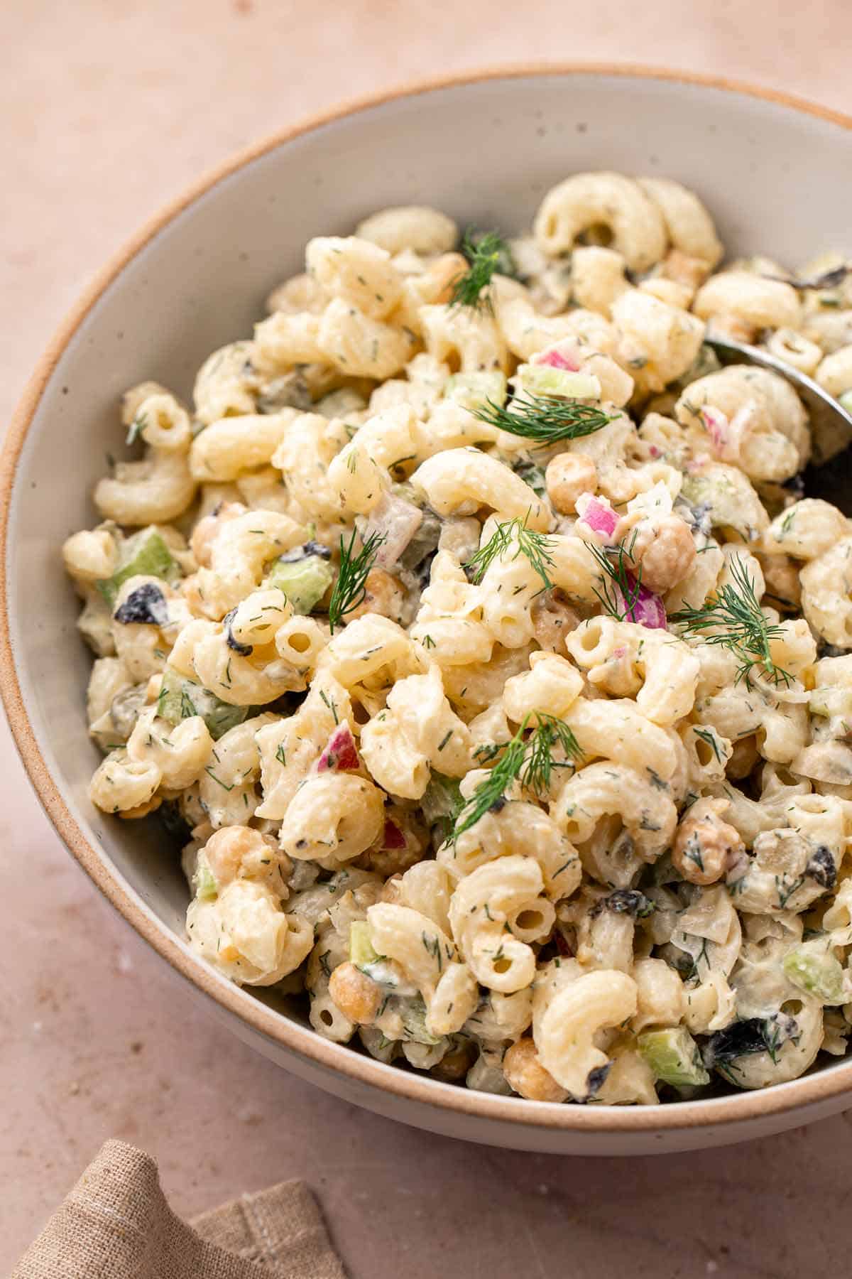 Creamy chickpea pasta salad with dill in a beige serving bowl