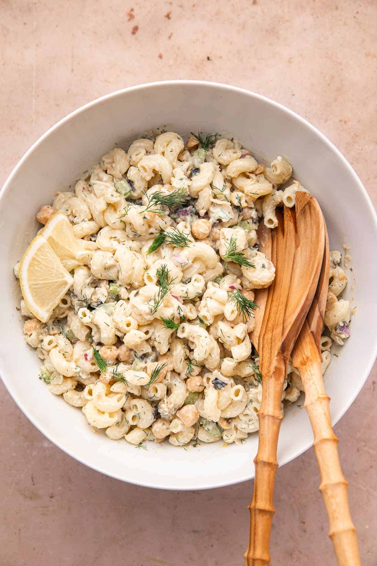 Vegan chickpea pasta salad with lemon slices and wooden salad servers