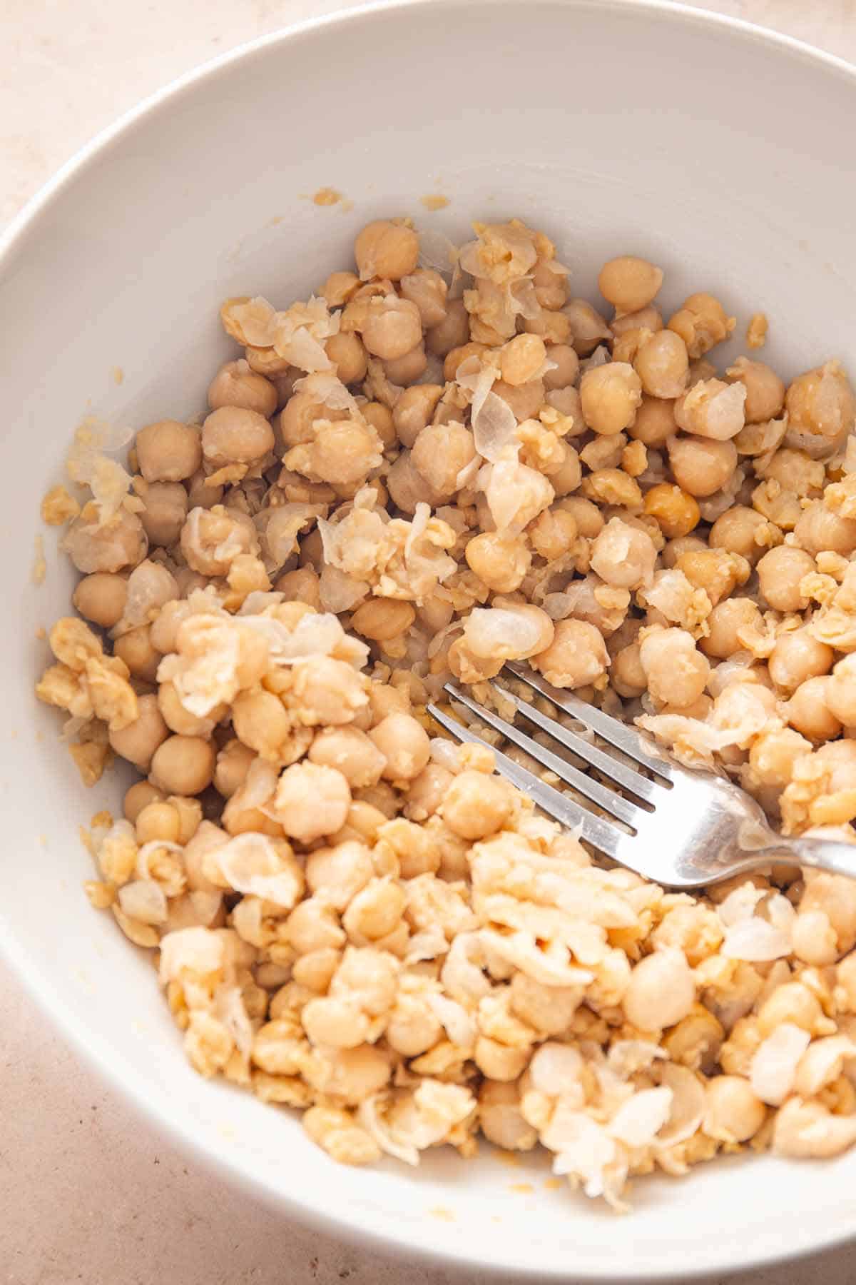 Mashed chickpeas in a bowl with a fork during recipe prep