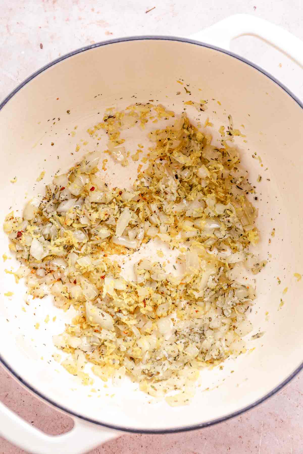 Diced onions and garlic sautéing in a pot with herbs