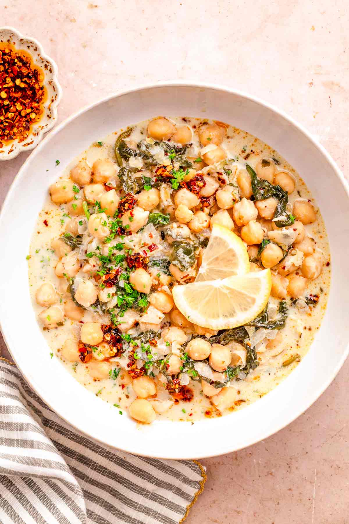 Bowl of creamy chickpea spinach stew with lemon wedges and chili oil