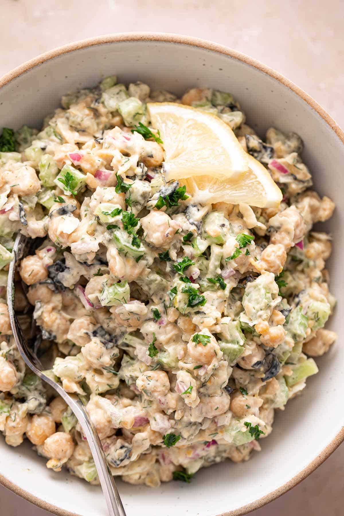 Creamy chickpea salad in a bowl with lemon slices and fresh parsley