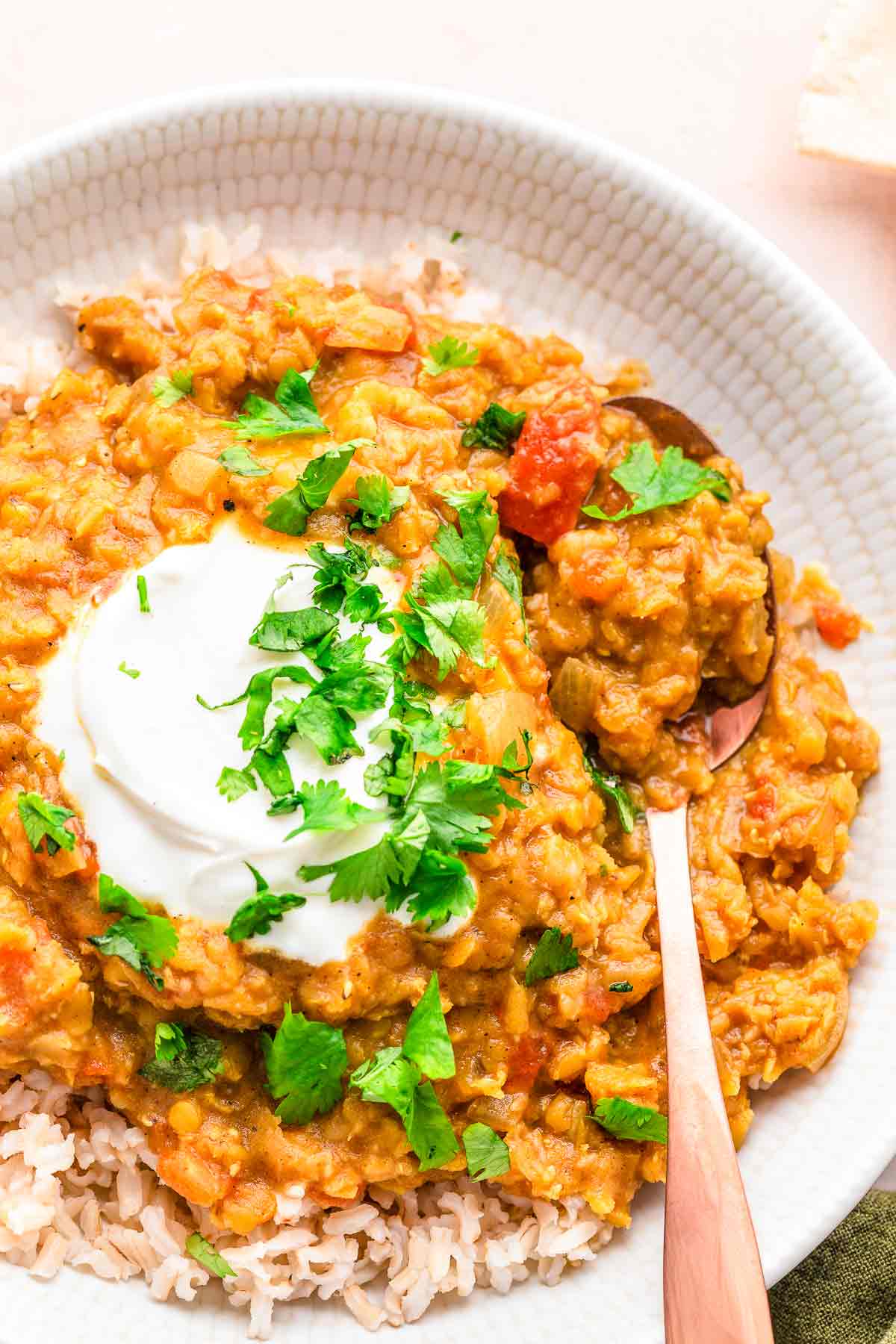 Bowl of red lentil dhal with rice, yogurt, cilantro, and spoon