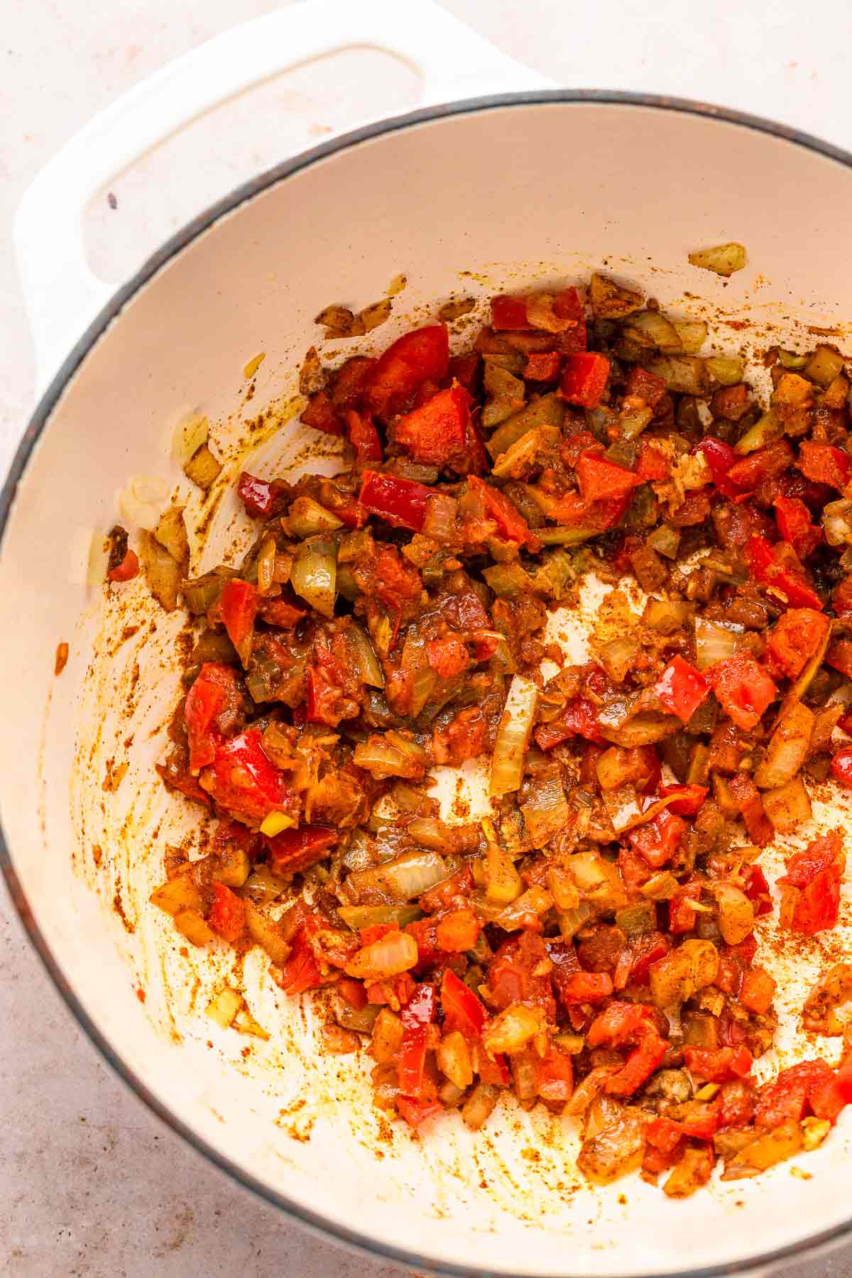 Sautéed onions, tomatoes, and spices cooking in a white pot