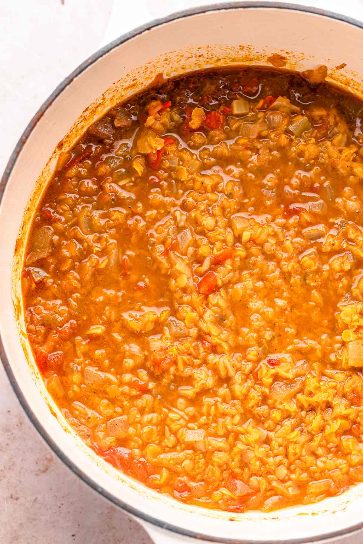 Red lentil dhal simmering in broth in a white cooking pot