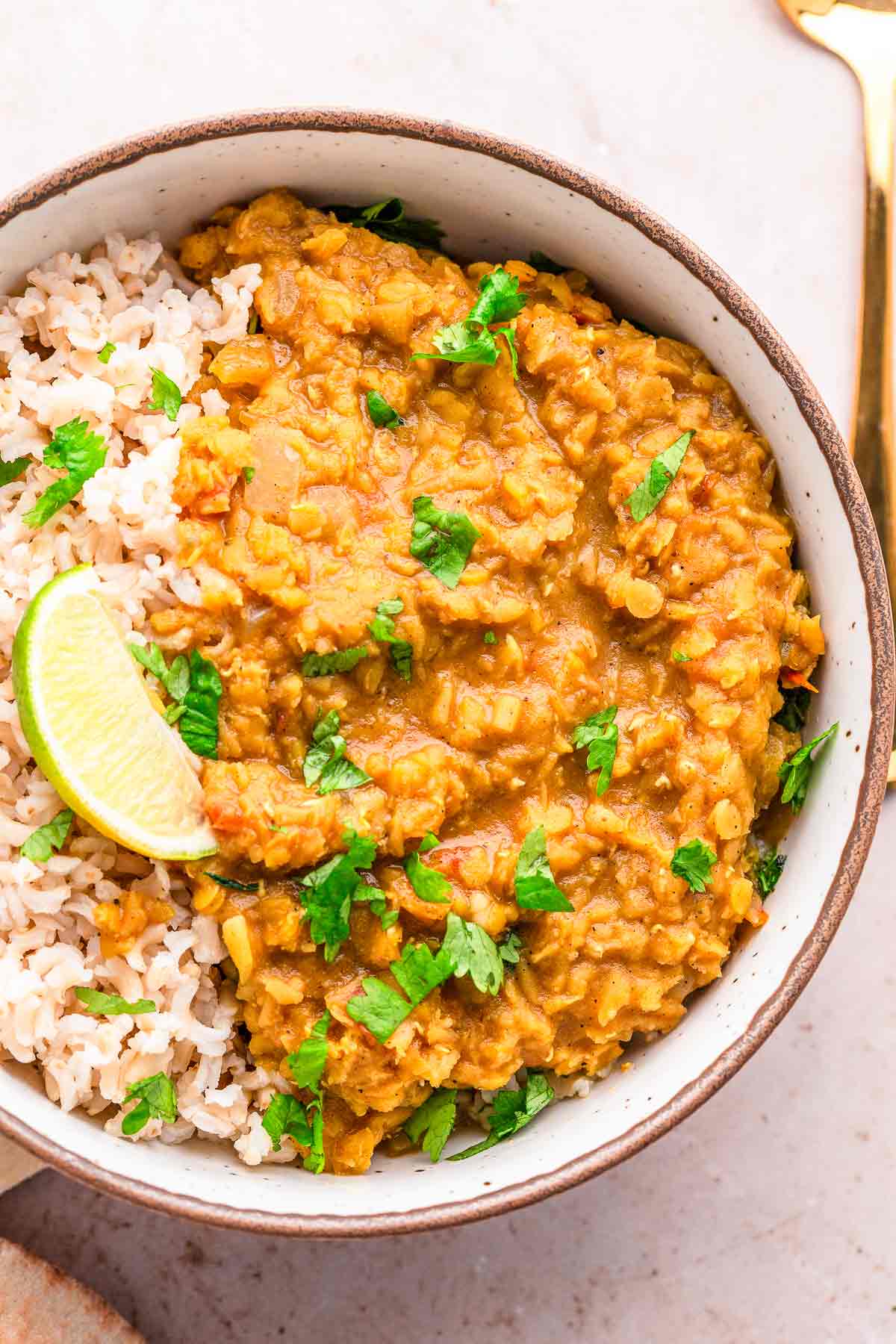Bowl of creamy red lentil dhal with rice, lime, and fresh cilantro