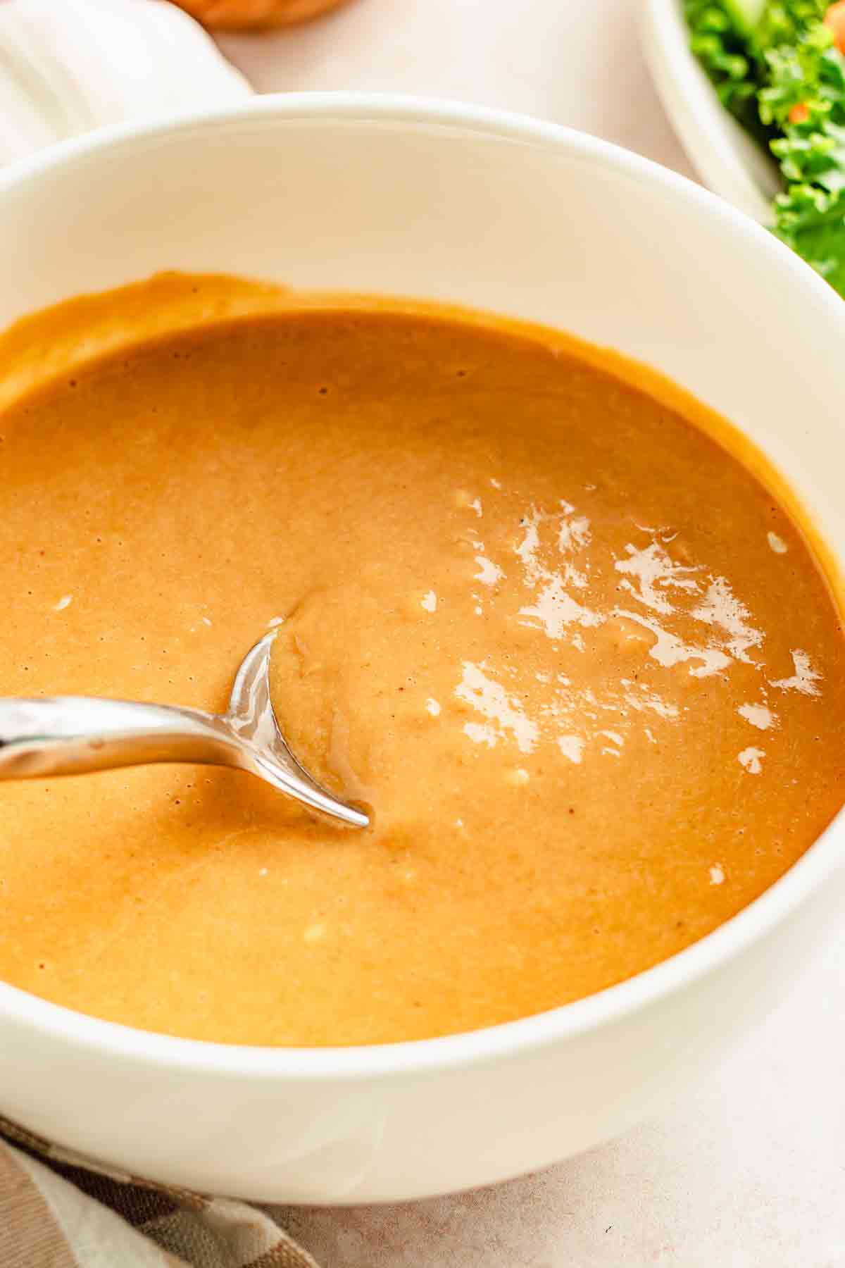 Spoon lifting creamy miso tahini dressing from a white bowl