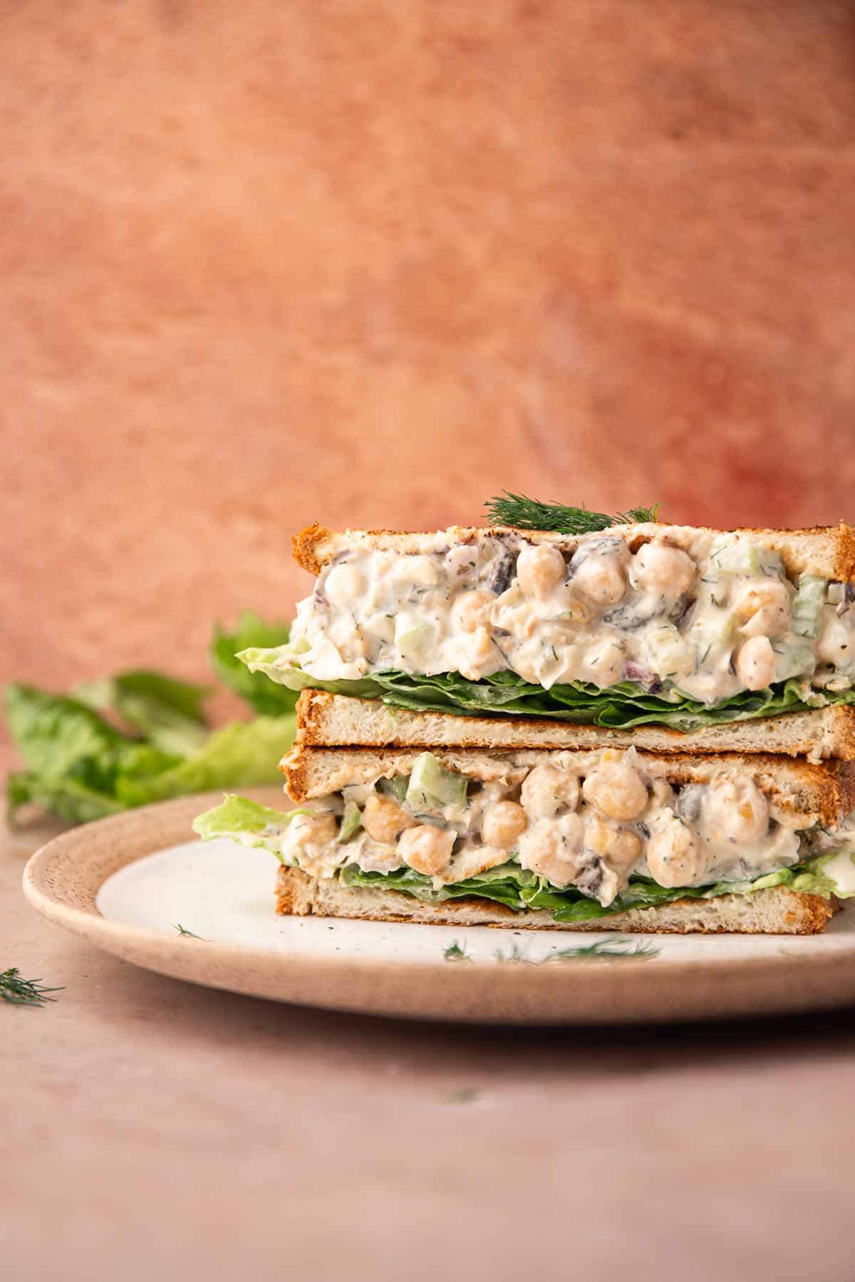 Chickpea salad sandwiches stacked on a plate with fresh lettuce layers
