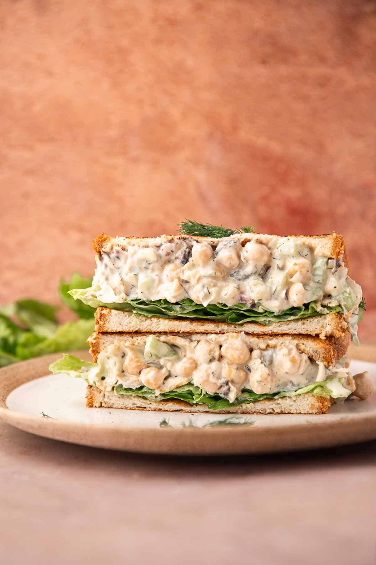 Stacked chickpea salad sandwiches on a plate with lettuce and dill garnish